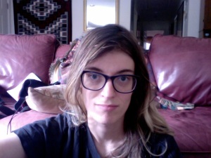 Image: Me, Beth, a 26-year-old thin, pale, white woman with blondish-brownish hair (with dark brown roots), purple glasses, dark eyebrows, dark blue eyes, and a black Beatles t-shirt. In the background is my parents' living room (a leather sofa and a Navajo rug are seen).